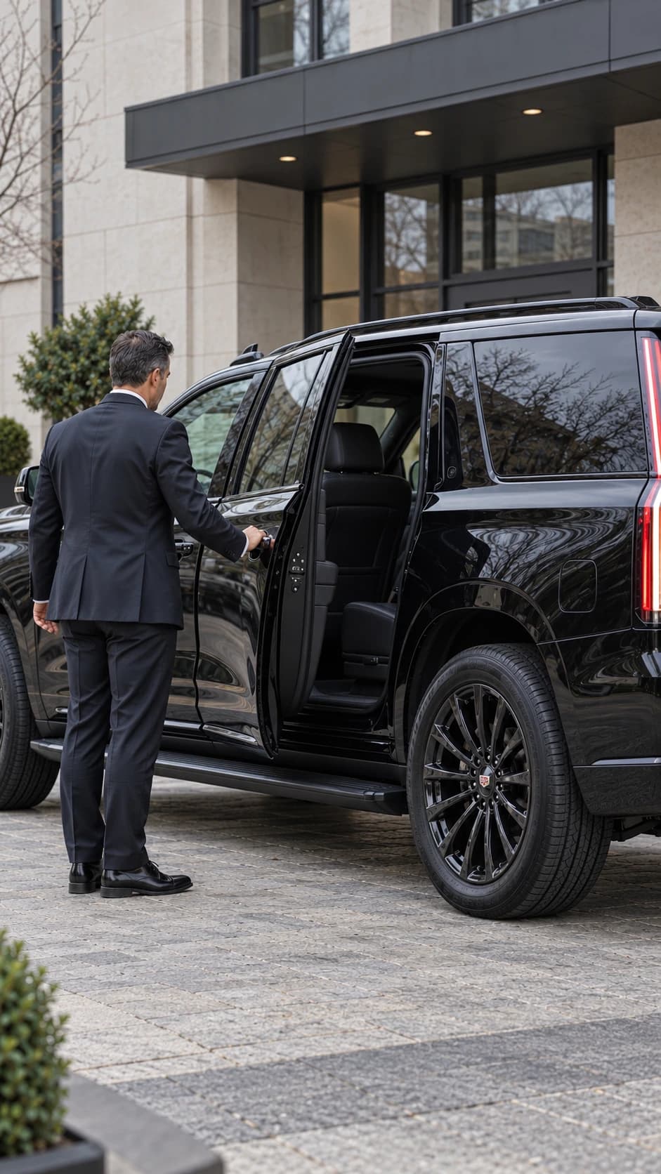 Chauffeur opening the rear passenger door of a black SUV