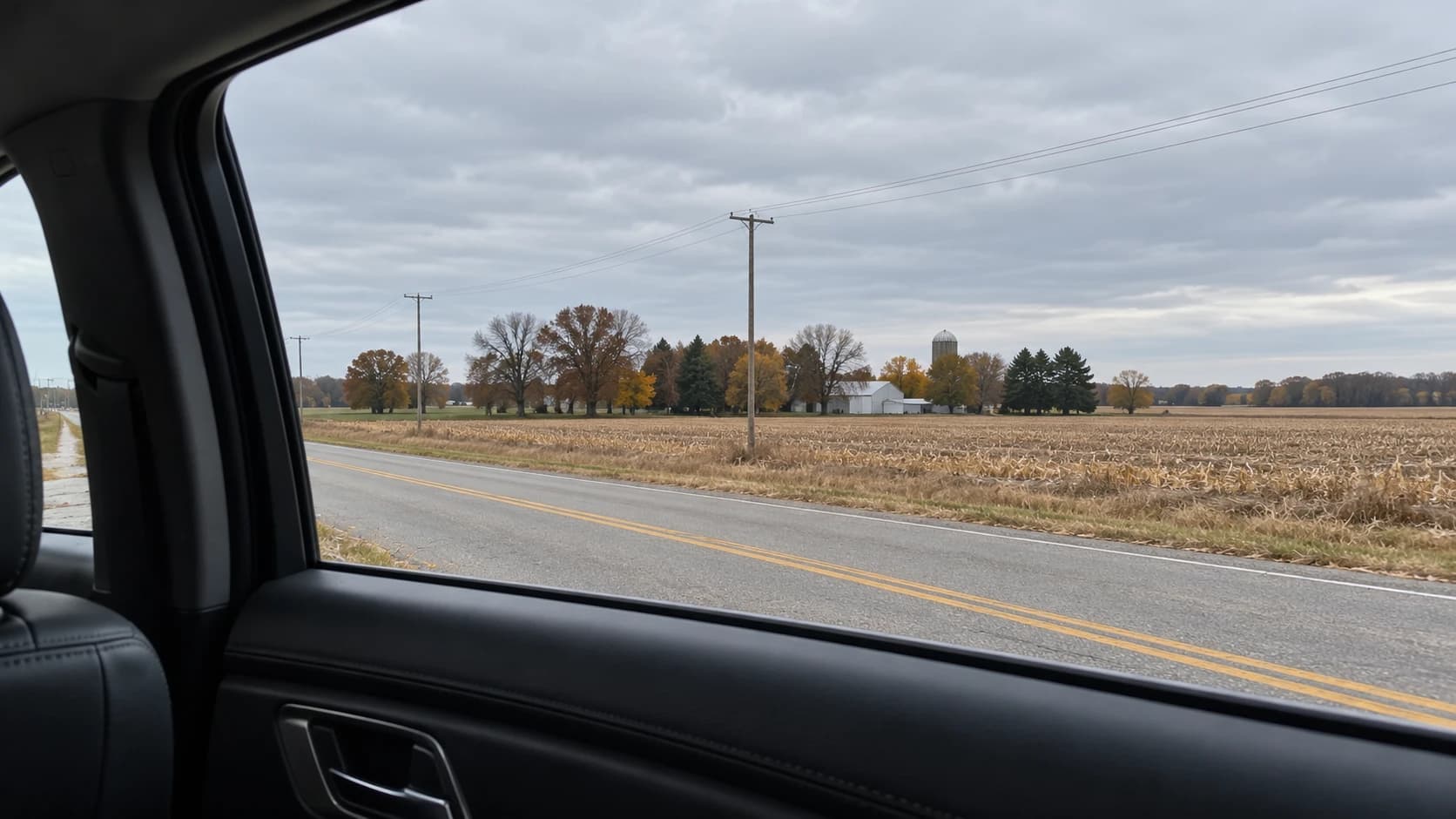 Quiet Midwestern road and fields seen through a passenger window